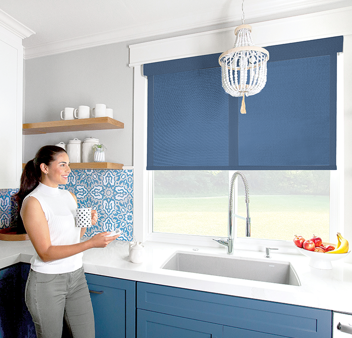 Woman in kitchen operating motorized shade behind the sink